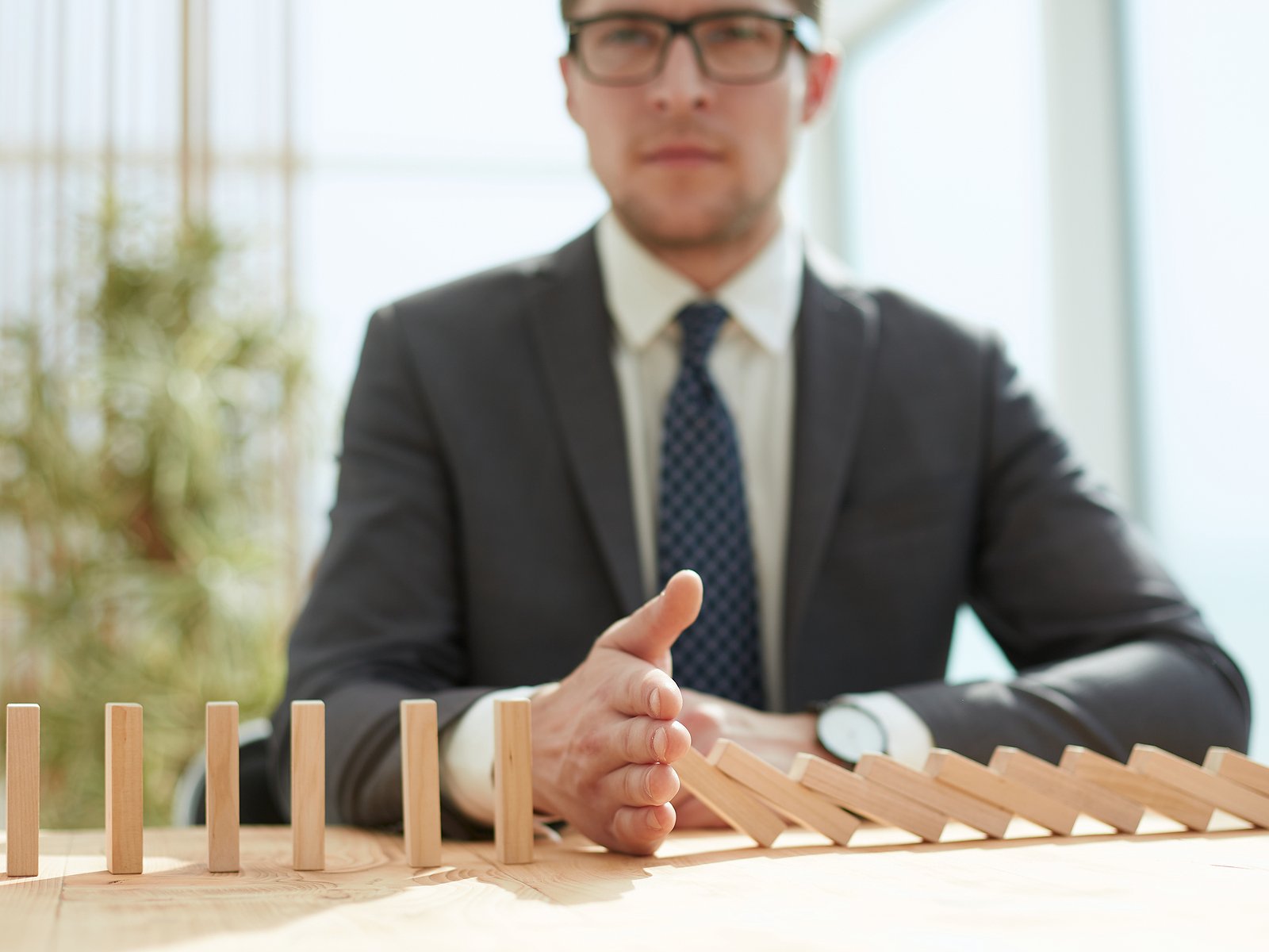 Businessman places hand between falling dominoes