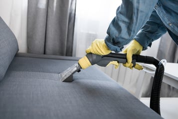 Person wearing rubber gloves uses machine to deep clean sofa.