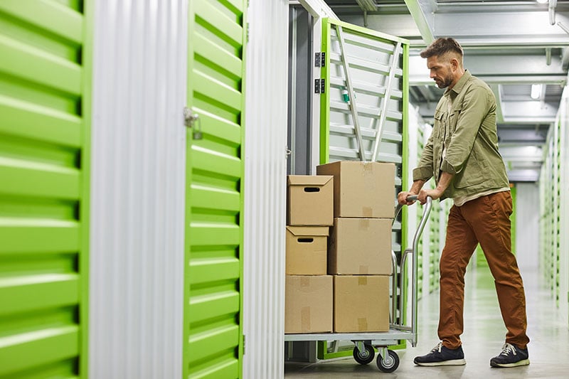Man pushing a cart loaded with boxes into a storage unit